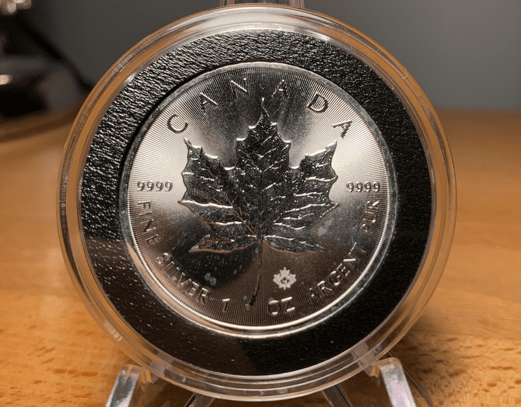 The obverse of a 2016 encapsulated silver maple leaf coin covered in milk spots.