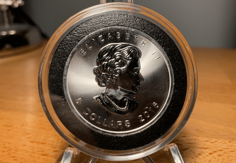 The obverse of a 2016 encapsulated silver maple leaf coin covered in milk spots.